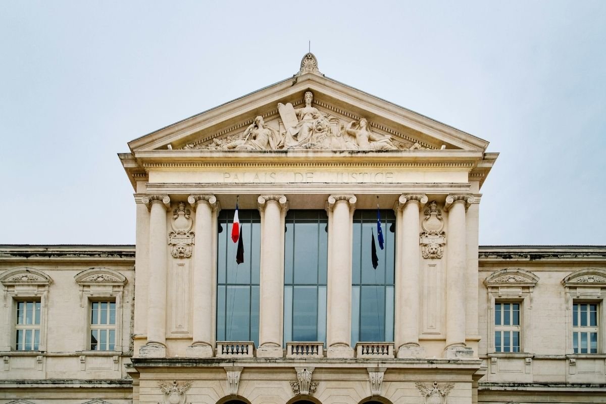 Façade d'un palais de justice français avec colonnes et drapeaux, symbole de l'accès public au droit