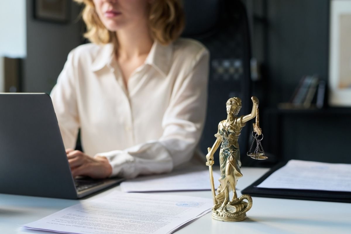 Femme remplissant une demande à son ordinateur, documents juridiques et statuette de la justice sur le bureau