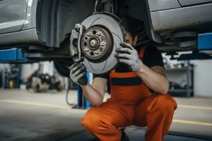 Technicien en combinaison orange inspectant les disques de frein d'une voiture surélevée lors d'une contre-visite au contrôle technique