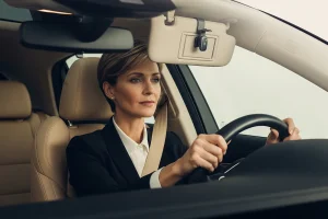 Conductrice les mains sur le volant avec un kit mains libres Bluetooth clip visible sur le pare-soleil, intérieur voiture